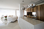 Eingebaute Küche mit Kücheninsel aus Marmor und weißes Designersofa vor Fenster in offenem Wohraum