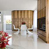 White designer chairs at glass table in front of wood-clad wall with TV cabinet in foreground