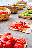 Rows of sliced homegrown tomatoes on wooden plates on burlap tablecloths with woven baskets lined up behind