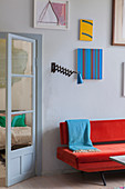 Red sofa below gallery of artworks next to glass door