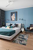 Double bed, mirrored bedside table and designer chair in bedroom with blue wall