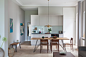 Dining table with slender lines and chairs in front of fitted kitchen in open-plan interior