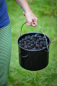 A woman carrying a pot of freshly picked blackberries