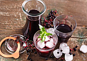 Homemade elderberry juice in glasses and carafes with ice cubes and mint
