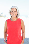 A mature woman with white hair on a beach wearing a red top