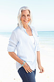 A mature woman with white hair on a beach wearing a striped blouse, a top and blue jeans