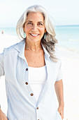Reife Frau mit weißen Haaren in gestreifter Bluse und Top am Strand