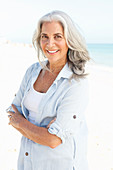 A mature woman with white hair on a beach wearing a striped blouse and a top