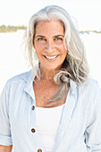 A mature woman with white hair on a beach wearing a striped blouse and a top