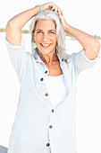 A mature woman with white hair on a beach wearing a striped blouse and a top