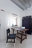 Wooden table and two chairs next to lattice window in front of black fabric wardrobe