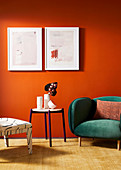 Chair, round table and armchair with green velvet upholstery against orange wall with pictures