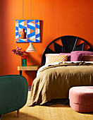 Doppelbett mit Betthaupt und Nachttisch vor orangefarbener Wand mit Bild