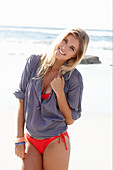 A blonde woman on a beach wearing a red bikini and a blue blouse