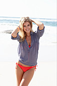 A blonde woman on a beach wearing a red bikini and a blue blouse