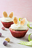 Two Easter bunny cupcakes with marshmallow ears in a pastel setting with mini eggs in the foreground