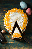 Round carrot cake with a slice cut decorated with candied orange peel