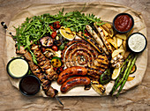 Grillplatte mit Fleisch, Wurst, Gemüse und verschiedenen Dips (Aufsicht)