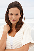 A brunette woman by the sea wearing a short-sleeved cardigan