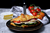 A croissant sandwich with cucumber, cheese, sausage and tomatoes