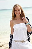 A young woman on a beach wearing a white summer dress and a striped cardigan