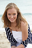 A young woman on a beach wearing a white summer dress and a striped cardigan