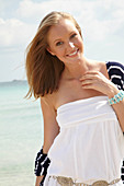 A young woman on a beach wearing a white summer dress and a striped cardigan