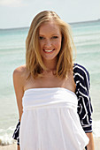 A young woman on a beach wearing a white summer dress and a striped cardigan