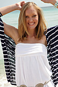 A young woman on a beach wearing a white summer dress and a striped cardigan