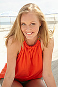 A blonde woman on a beach wearing an orange top