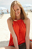 A blonde woman on a beach wearing an orange top