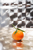Mandarine mit Blatt vor spiegelndem Hintergrund