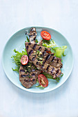 Chargrilled lamb liver slices on salad greens and grilled plum tomatoes