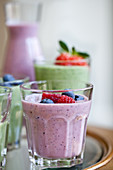 Berry smoothies and green smoothies in various cups and carafes, topped with fruit