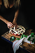 Crop shot of woman creating lattice top pie crust with straps of dough covering form with filling