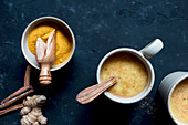Bowl with turmeric and cinnamon with ginger lying near cups of fresh latte on dark tabletop