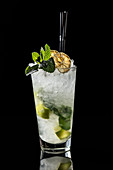 High glass with traditional Mojito cocktail garnished with dried lime and mint on black background