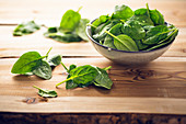 Fresh spinach leaves in a bowl and on a wooden table