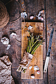 A bunch of green asparagus, garlic bulbs, and a knife on a wooden table