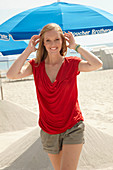Blonde Frau in rotem Top und Shorts am Strand