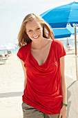 A blonde woman on a beach wearing a red top and shorts