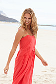 A young blonde woman on a beach wearing a red summer dress