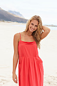 A young blonde woman on a beach wearing a red summer dress