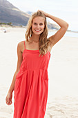 A young blonde woman on a beach wearing a red summer dress