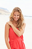 A young blonde woman on a beach wearing a red summer dress