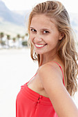 A young blonde woman on a beach wearing a red summer dress