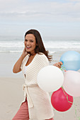 A brunette woman wearing a short-sleeved cardigan and holding balloons