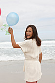 A brunette woman wearing a short-sleeved cardigan and holding balloons