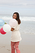 A brunette woman wearing a short-sleeved cardigan and holding balloons