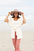 A brunette woman wearing a short-sleeved cardigan and a hat